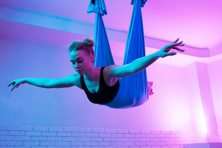 迷人的健康年轻女子做飞行瑜伽伸展吊床在瑜伽工作室。