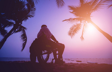 沙滩上坐轮椅的残疾人。日落时的剪影。