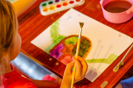 学龄前女孩在纸上用明亮的颜料画水彩画，特写。儿童家庭教育