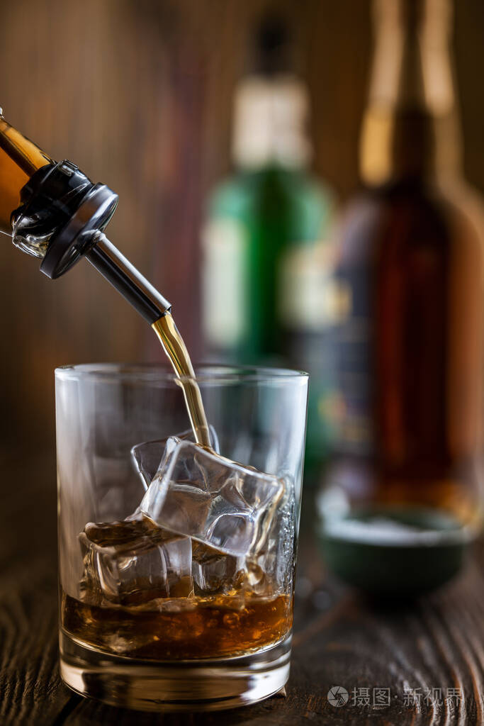 在酒吧里威士忌被倒进一个装有冰块的玻璃杯里背景中有酒瓶放在吧台的