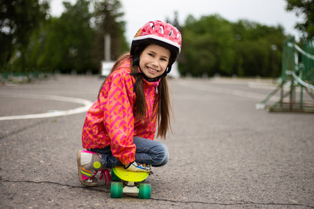 可爱的小女孩骑在美丽的夏季公园的滑板上