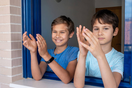 在冠状病毒covid19大流行隔离期间,孩子们开心地笑着拍手,从窗口鼓掌