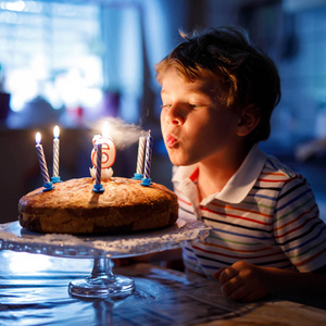 可爱的快乐的金发小男孩庆祝他的生日。孩子在自制的烤蛋糕上吹蜡烛，室内。学校儿童生日聚会，家庭庆祝6年