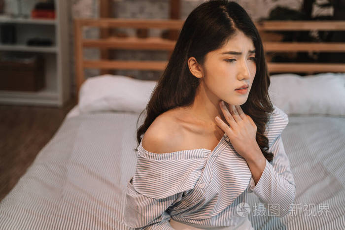 一幅20多岁的亚洲年轻女子的画像晚上在卧室里忍受疼痛和疾病的折磨