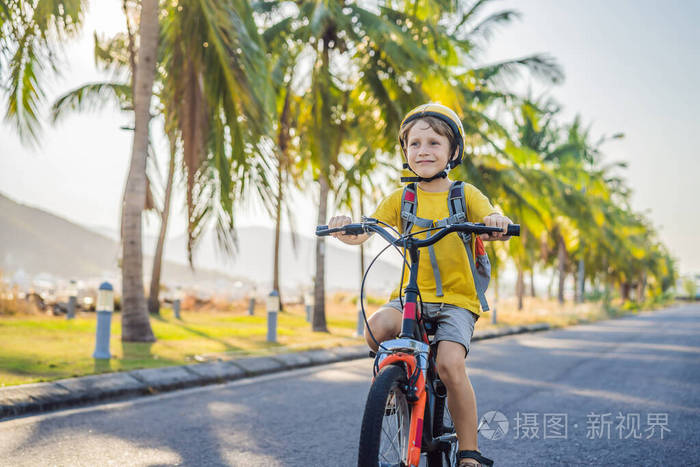 在阳光明媚的日子里，戴着安全帽骑着自行车背着背包的活跃的学校男孩。快乐的孩子在上学的路上骑自行车。孩子们在户外上学的安全通道