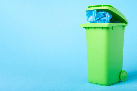 蓝色背景上有聚乙烯废料的绿色垃圾桶，并有放置文本的地方