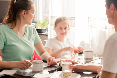 一个幸福的家庭在他们公寓厨房的桌子上吃早餐。厨房阳光明媚。