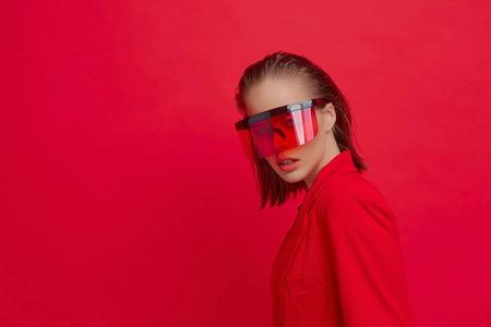 一个酷酷时尚的女孩，发型时尚，戴着大玻璃的时髦眼镜，在鲜红色的背景下摆出姿势