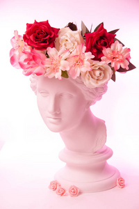 美丽的年轻女性白脸和五颜六色的花朵。把维纳斯的古董半身像贴在花环里。美丽的春夏模特儿带着清新的花束。