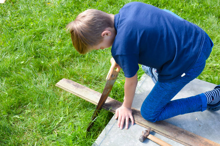 男孩在锯木头。一个男孩在花园里工作。外面的儿童工作室