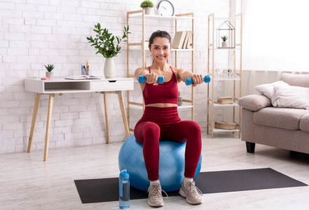千禧一代女孩在客厅用哑铃和健身球锻炼身体照片