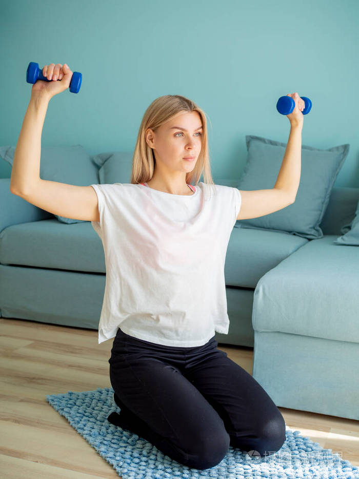 在家锻炼美丽的女人坐在地板上举着一个两个哑铃室内垂直拍摄