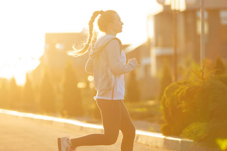 在阳光都市里跑步的是年轻的女运动员.美丽的白人女子训练,听音乐照片