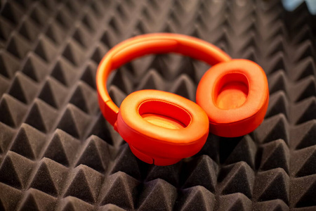 橙色无线头戴式耳机位于黑色泡沫橡胶消音板上。特写软聚焦，模糊背景。