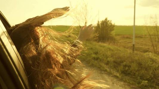 留着长发的女孩坐在汽车的前排座位上,伸出手臂,捕捉落日的耀眼光芒