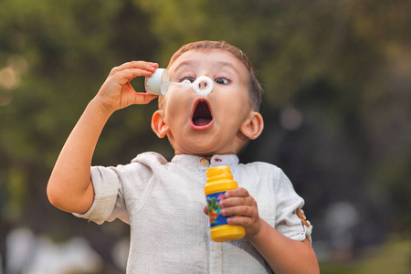 一个张大嘴巴和大眼睛的孩子在大自然里吹着五颜六色的肥皂泡。