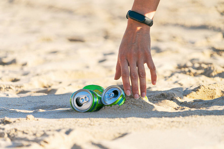 清理海滩上的垃圾。从海滩上捡空的软饮料罐垃圾的女人的手