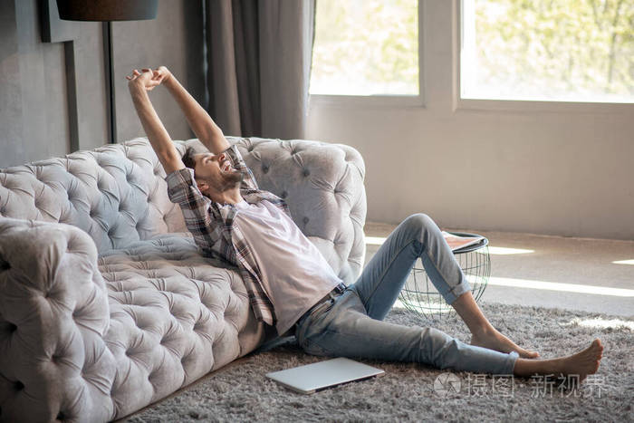 有胡子的男人坐在地板上打哈欠伸懒腰