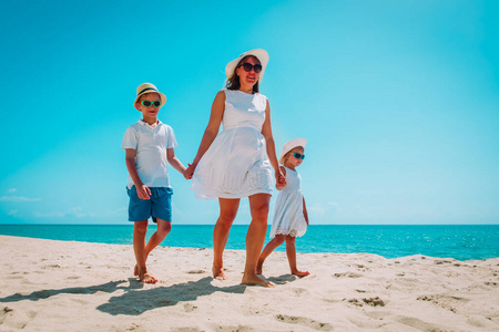 母亲带着儿子和女儿在沙滩上散步