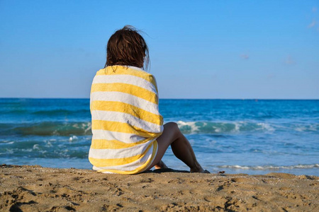 成熟的美女拿着沙滩巾坐在沙滩上，女人在欣赏海上夕阳景观