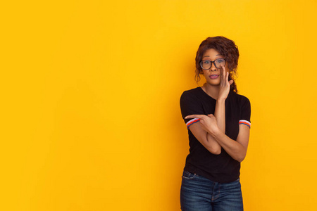 非洲裔美国人美丽的年轻女性肖像画在黄色的工作室背景上，富有情感和表现力。广告文案空间。