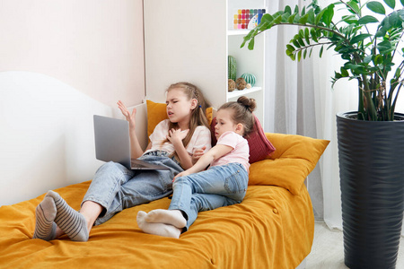 Two sisters lying on a bed together using laptop watching someth