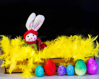 Easter bunny, coloful eggs and yellow feathers on black backgrou