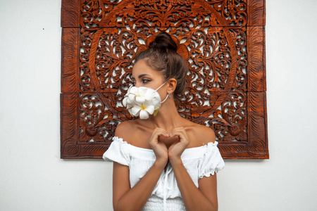  Girl in a mask of fresh flowers. Hand gesture depicts the heart