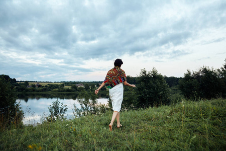 一个女孩沿着一片郁郁葱葱的草地跑到池塘边