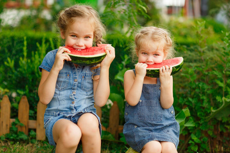 Little girls sit on watermelon and eating pieces 