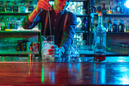 酒吧男招待的特写镜头在五彩缤纷的霓虹灯下完成了酒精和冰鸡尾酒的准备