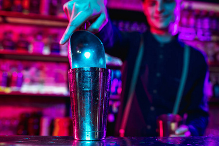 酒吧男侍者的特写镜头在五彩霓虹灯下完成了酒精鸡尾酒的准备