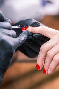 特写镜头在美容院里，戴着橡胶手套覆盖着红指甲的大师。完美的指甲修剪过程。凝胶抛光概念。
