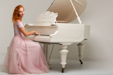 美丽的年轻女子在一架白色的大钢琴旁。