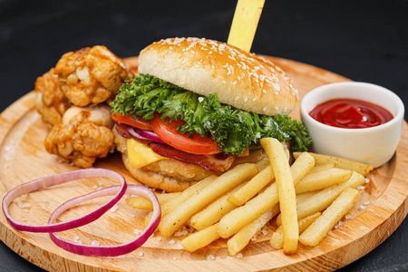 多汁的汉堡包,炸薯条,鸡腿和沙司.提供黑色背景的木板和餐具.快餐店.