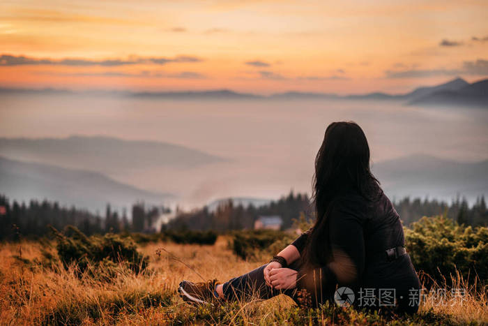一个女人坐在山顶上等待太阳升起