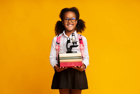 快乐的非洲女孩拿着书和显微镜学习，黄色背景