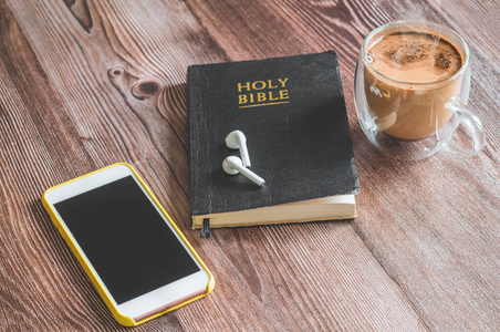 The Holy Bible with headphones, a phone and a hot cup of coffee.