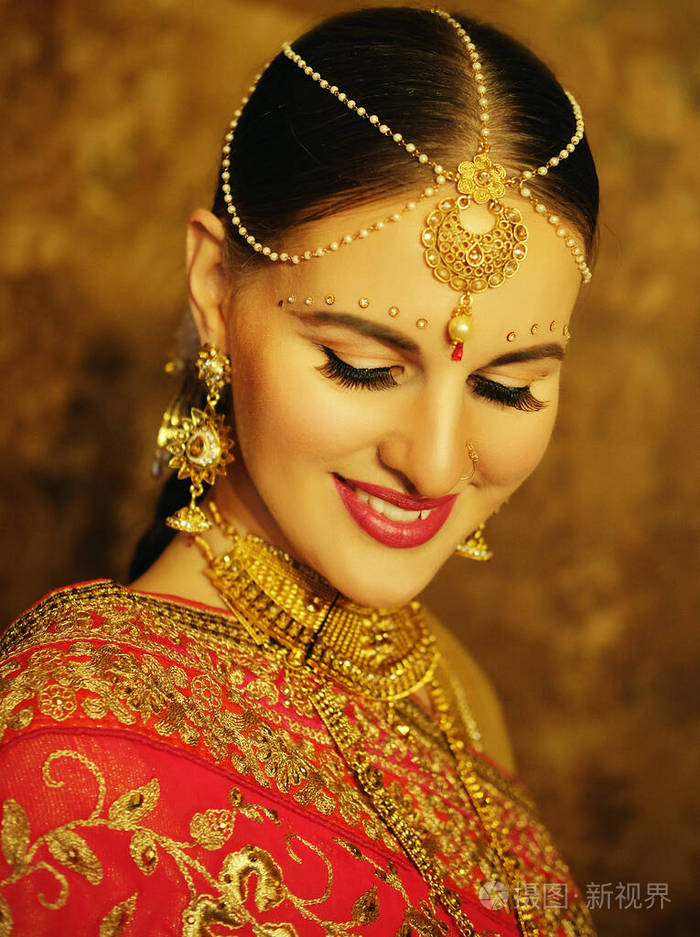 美丽的印度女孩在家微笑的肖像戴着金首饰的年轻女模特