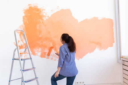 兴高采烈的女人在粉刷新家的墙壁。翻新修理和重新装修概念。