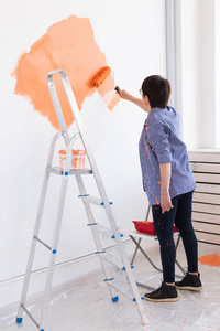 在公寓里修理。快乐的中年妇女用油漆粉刷墙壁。