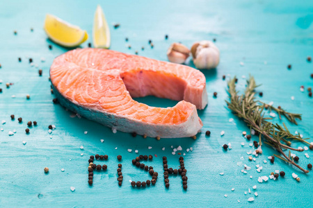 新鲜鲑鱼鱼片在蓝色背景俯视图和铭文胡椒鱼，食物特写。饮食，欧米茄维生素和海鲜概念。