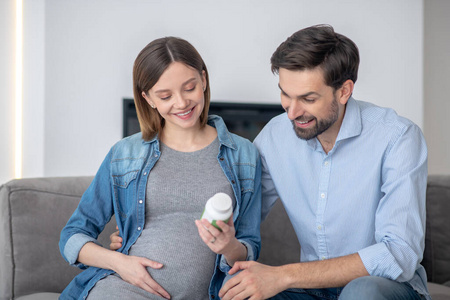 年轻的孕妇微笑着向丈夫展示一瓶维生素