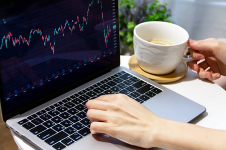 交易员正坐在家里的桌子旁,用黑色显示器显示图形图表的笔记本电脑