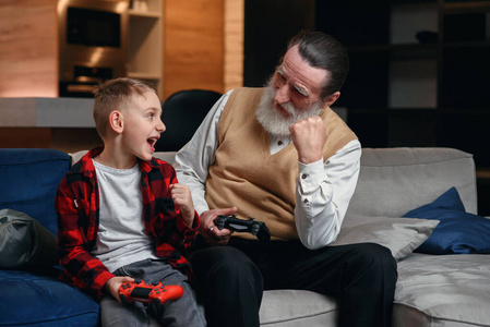 可爱的小男孩和爷爷坐在沙发上玩游戏机