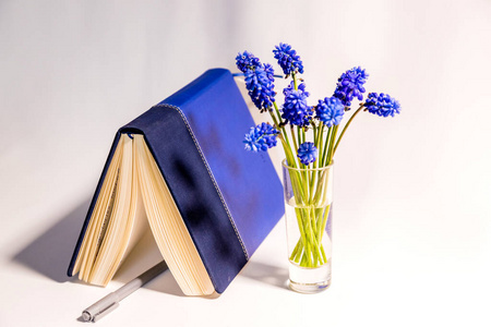 白色的桌子上有蓝色的花朵，日记本上有钢笔俯视图