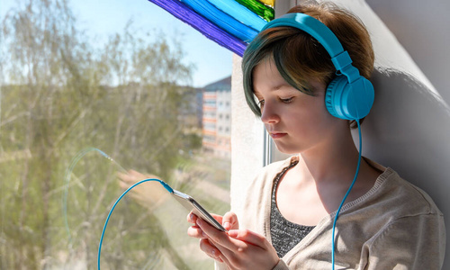 悲伤音乐悲伤的少女戴着耳机听着音乐,靠在窗户上.想念她的朋友.照片