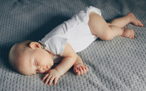 睡梦中的男婴穿着白色连体衣躺在床上