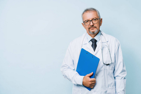 上了年纪的大胡子男医生，穿着白色制服，带着一个蓝色文件夹的听诊器。医学研究实验室背景的医生。