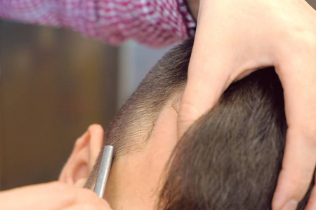 理发师用锋利的剃须刀在男人的太阳穴上刮头发.造型师手特写.照片